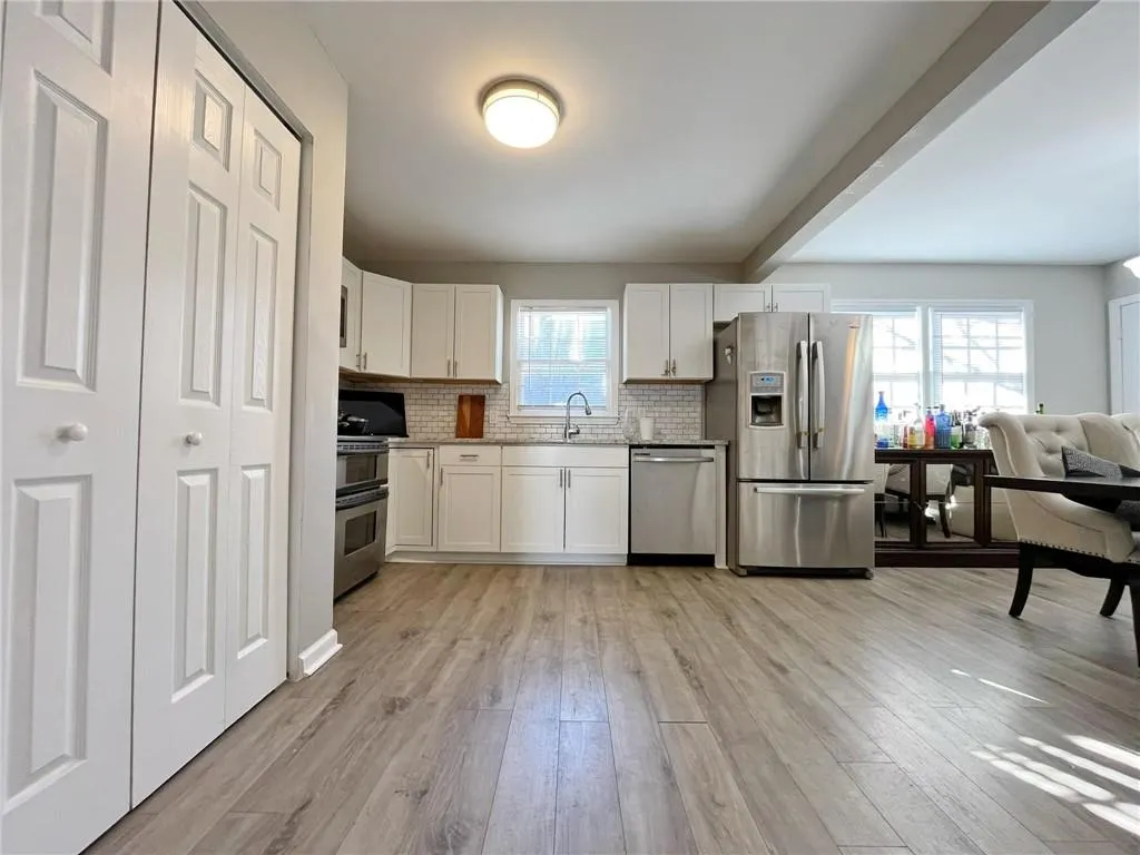 Kitchen with stainless steel appliances, white cabinetry, beamed ceiling, light wood-type flooring, and backsplash