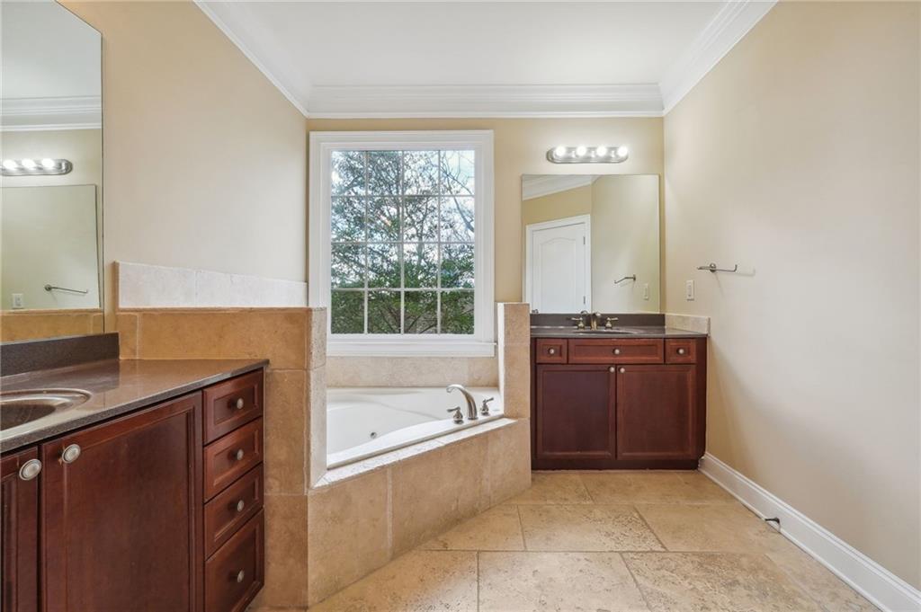 Bathroom with tiled tub, crown molding, vanity with extensive cabinet space, double sink, and tile floors