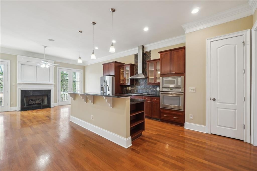 Kitchen with wall chimney exhaust hood, stainless steel appliances, ceiling fan, and hardwood / wood-style floors