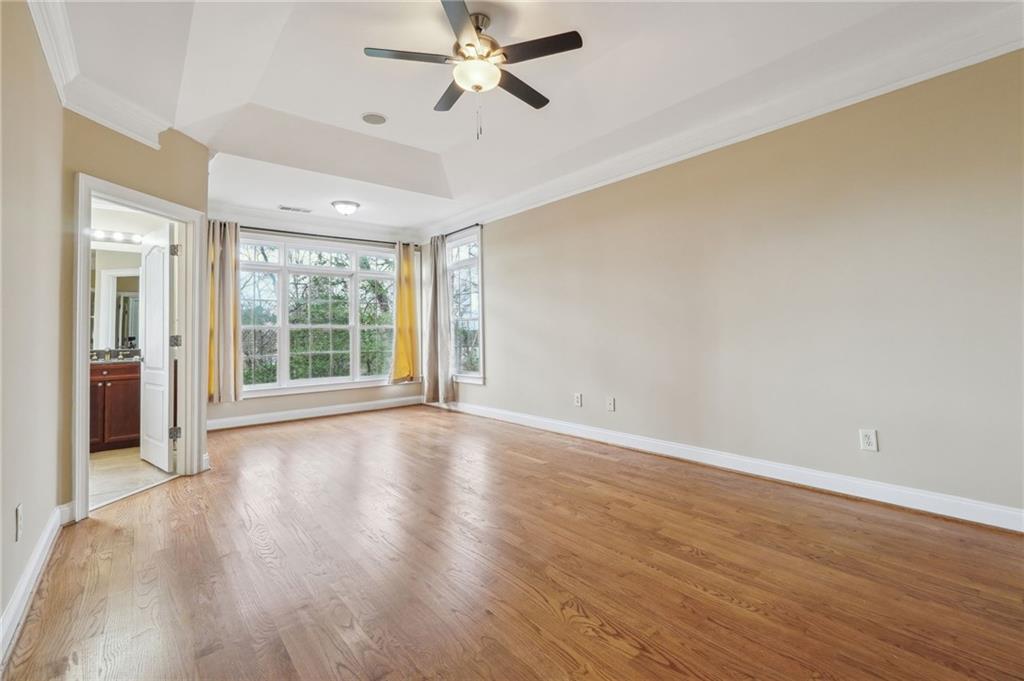 Unfurnished room featuring a raised ceiling, ornamental molding, ceiling fan, and light wood-type flooring