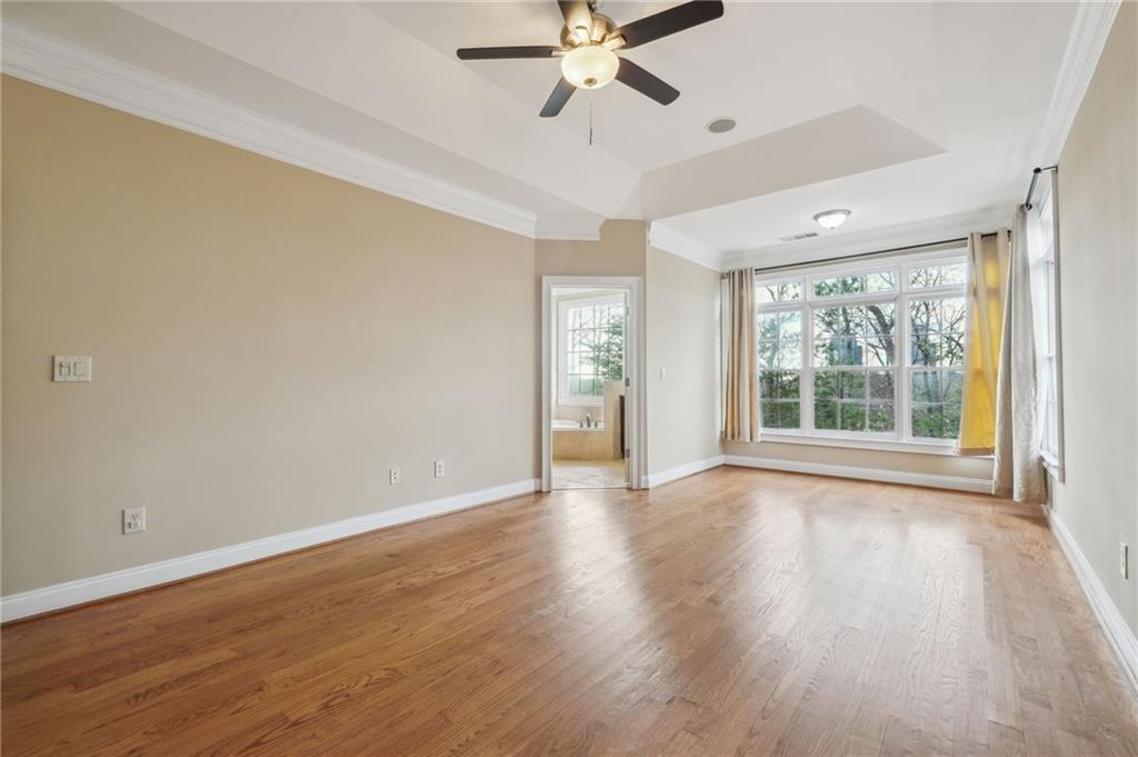 Unfurnished room with light wood-type flooring, crown molding, ceiling fan, and a raised ceiling