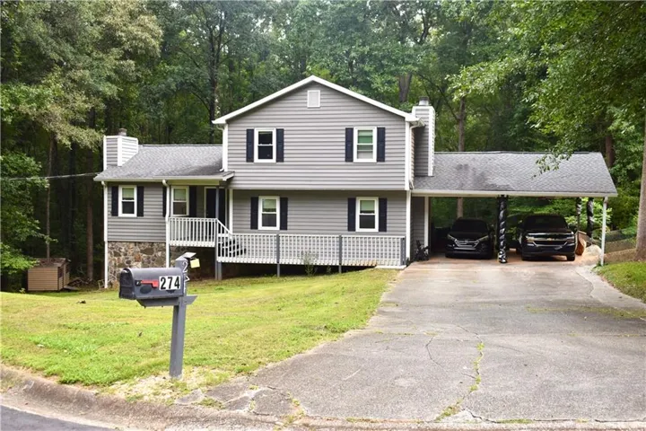 Gray siding exterior with a partial stone foundation, black window shutters, and a covered carport