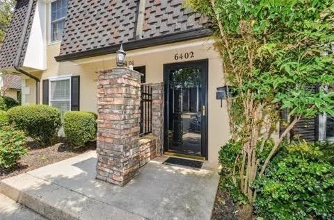 Paved entry leading to a dark-framed glass door, flanked by a brick and wrought iron column