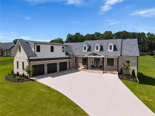 Brick and vertical siding exterior with a dark gray shingle roof, three dormer windows, and a three-car garage