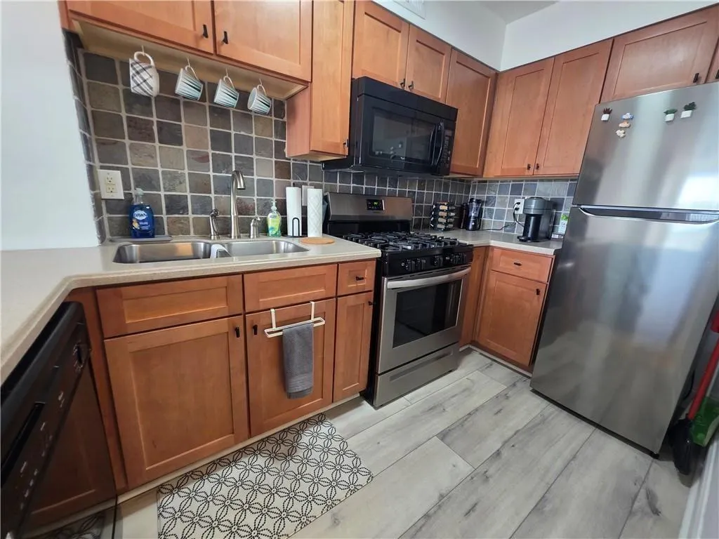 Kitchen with black appliances, decorative backsplash, and brown cabinetry
