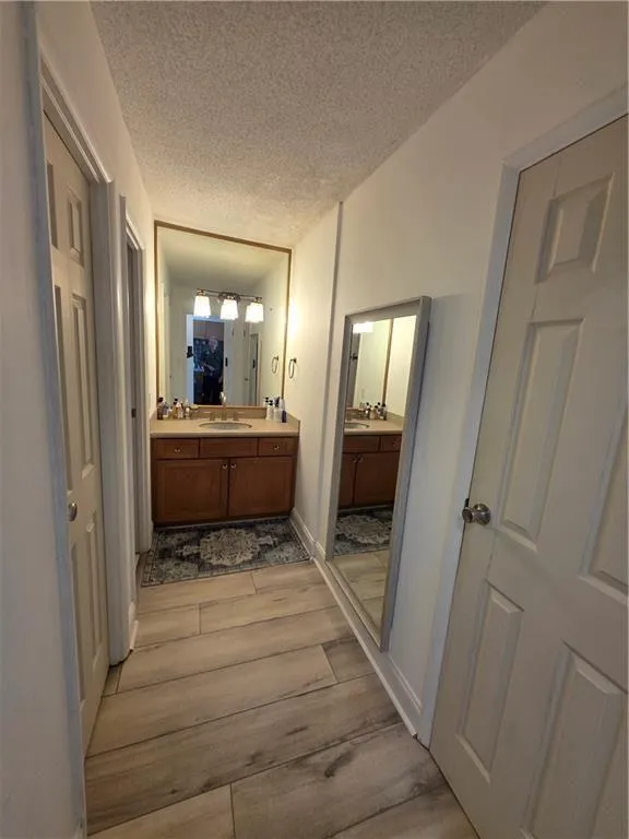 Full bathroom with double vanity, a textured ceiling, and light wood finished floors
