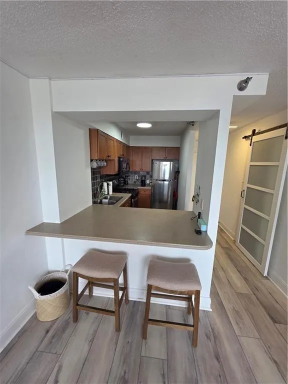Kitchen featuring a barn door, a kitchen bar, brown cabinets, appliances with stainless steel finishes, and light wood finished floors