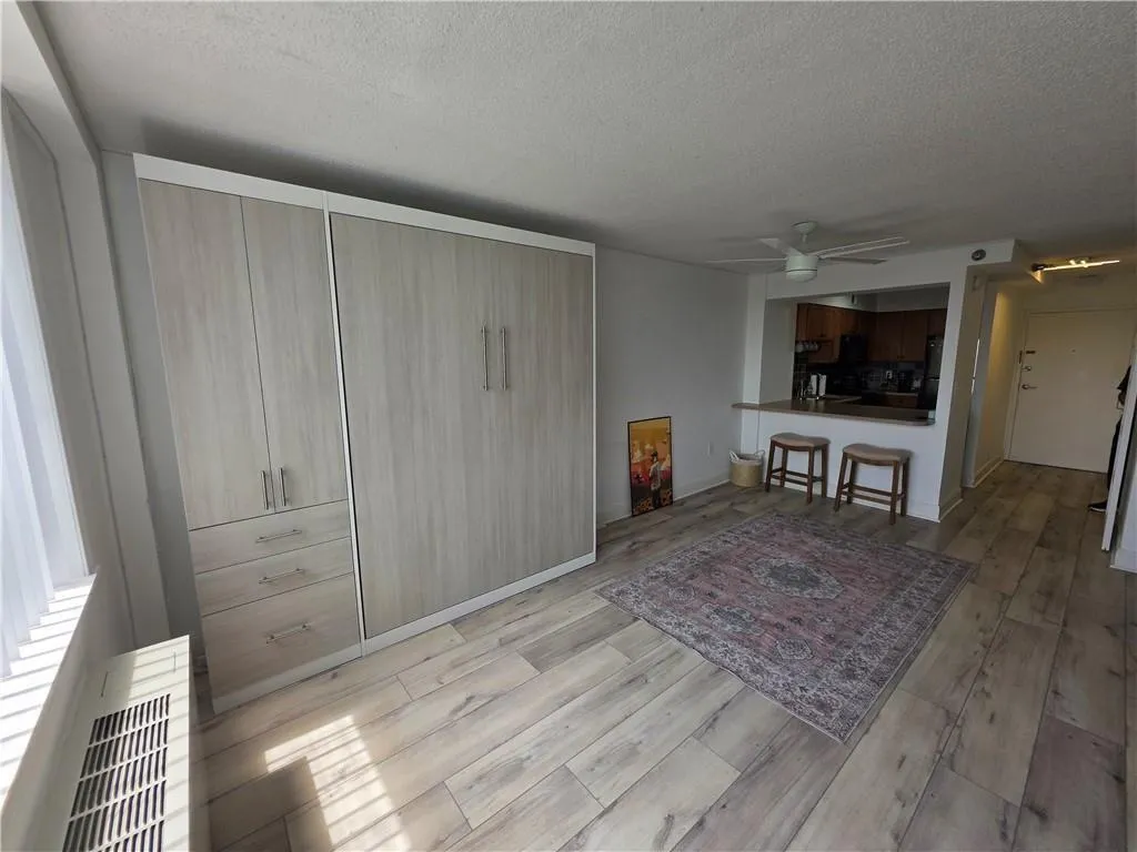 Living area featuring a textured ceiling, light wood finished floors, ceiling fan, and radiator heating unit