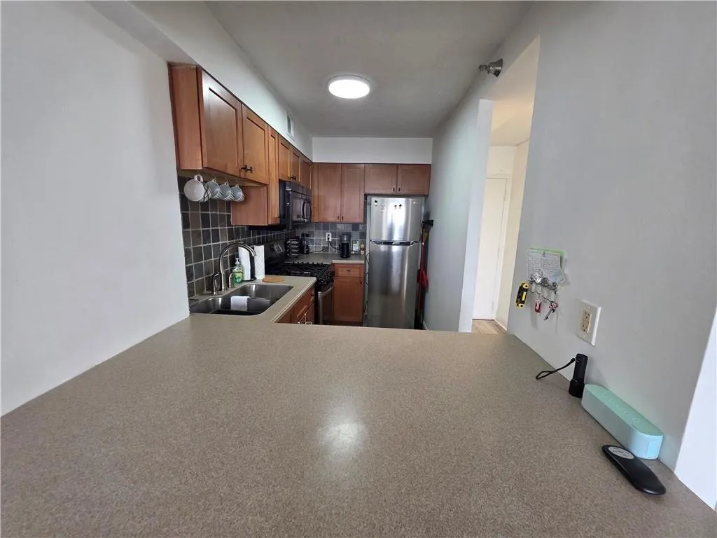 Kitchen featuring backsplash, stainless steel appliances, brown cabinets, and light countertops