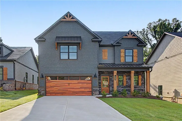 Two-story residence featuring a charcoal-gray fiber cement exterior with contrasting wood-finish garage doors, multiple gabled rooflines with metal accents, and warm-toned window frames