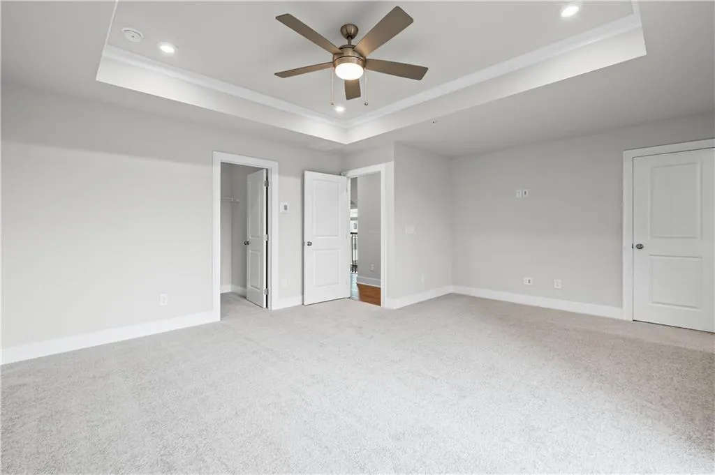 Primary bedroom featuring a tray ceiling, light colored carpet, recessed lighting, ceiling fan, and two large walk-in closets