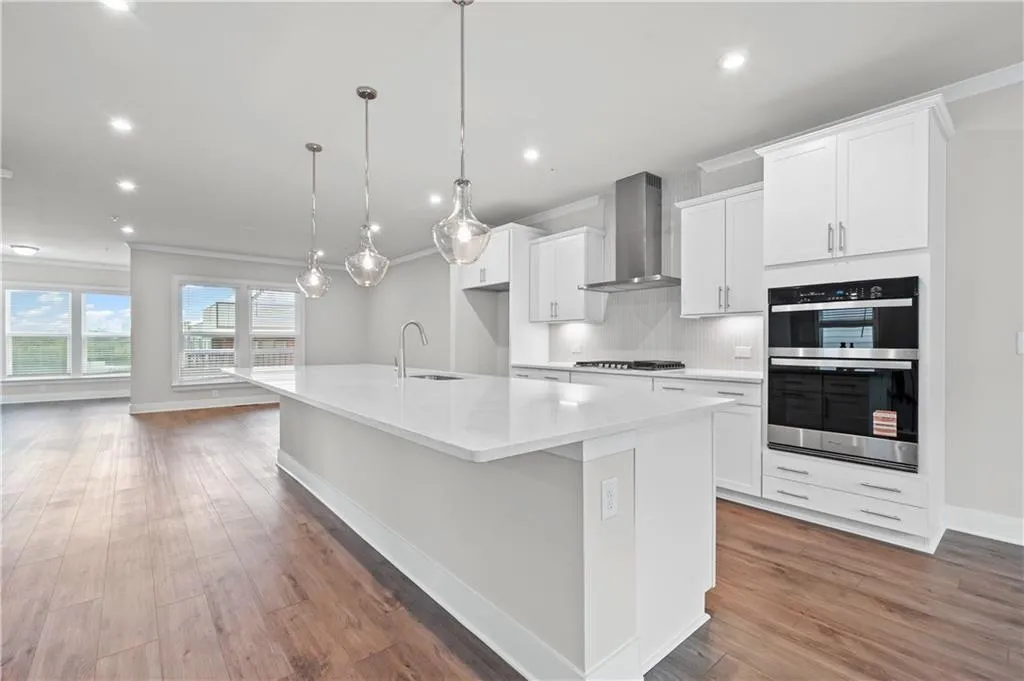 Kitchen featuring white cabinets, double oven, crown molding, a kitchen island with sink, and decorative backsplash