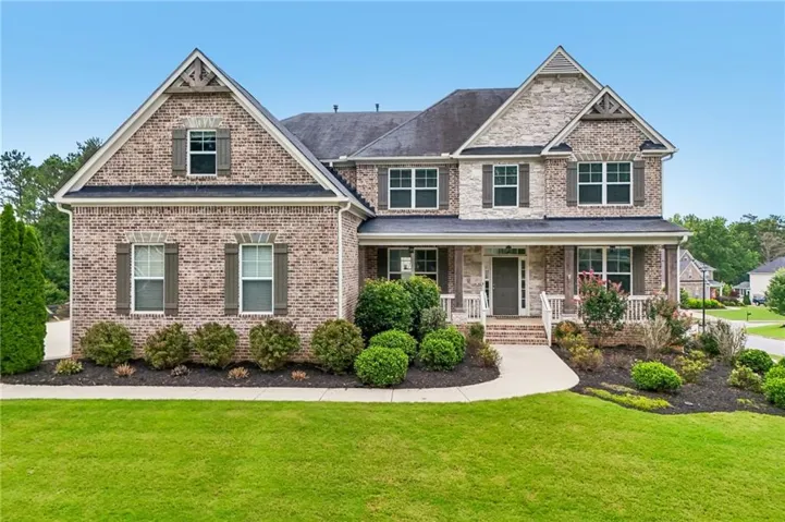 Brick and stone façade residence featuring a covered front porch, white railings, and dark shutters