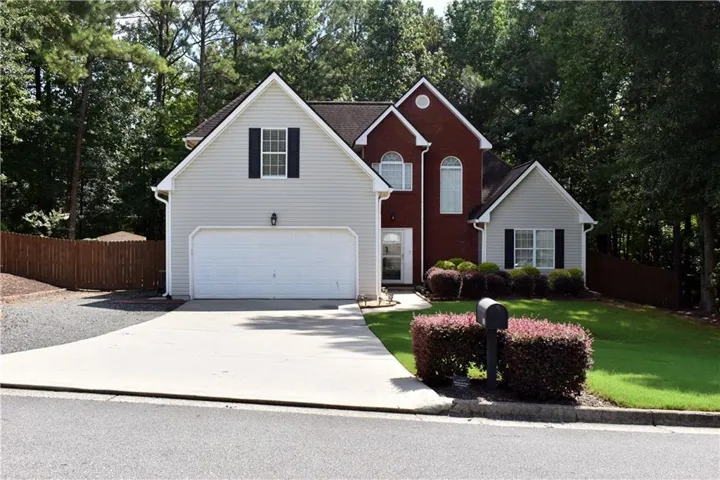Two-story residence featuring a brick and siding facade, an attached garage, a paved driveway, mature landscaping, and a fenced side yard