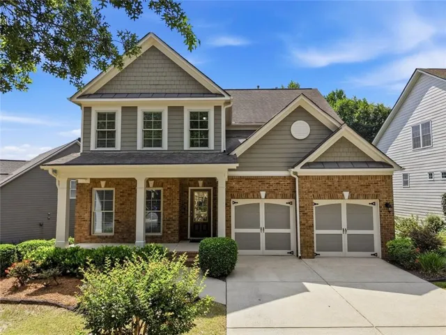 Traditional-style residence featuring a brick and siding exterior, a covered front porch with white columns, and a two-car garage with arched doors