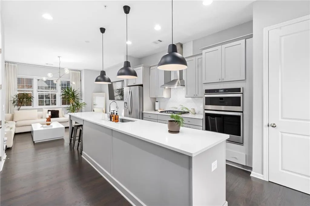 Kitchen featuring decorative backsplash, dark wood-style flooring, a kitchen island with sink, stainless steel appliances, and decorative light fixtures
