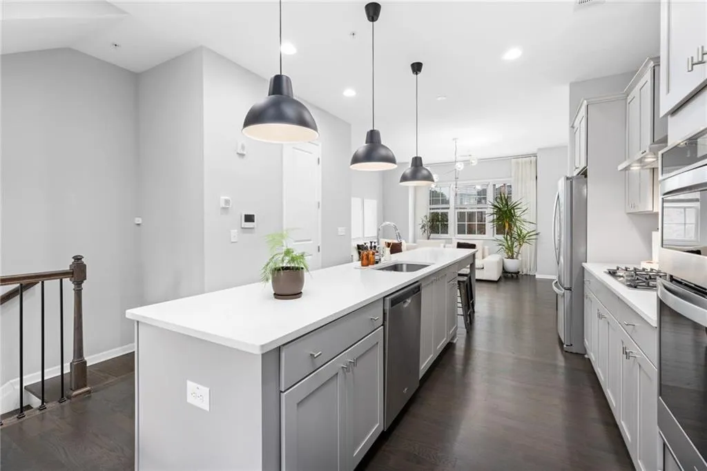 Kitchen with dark wood-style floors, hanging light fixtures, appliances with stainless steel finishes, an island with sink, and gray cabinets