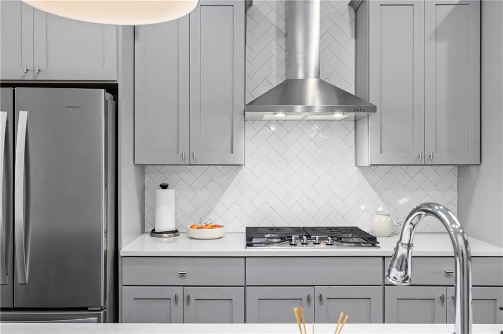 Kitchen with gray cabinets, appliances with stainless steel finishes, and wall chimney range hood