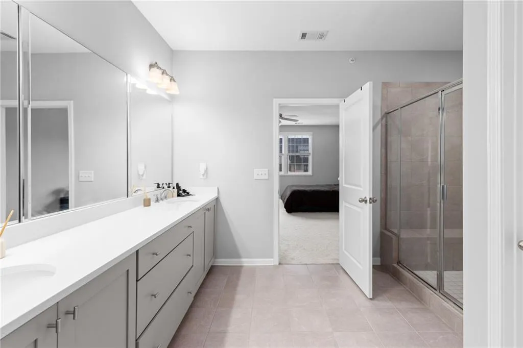 Ensuite bathroom with double vanity, a shower stall, and light tile patterned floors