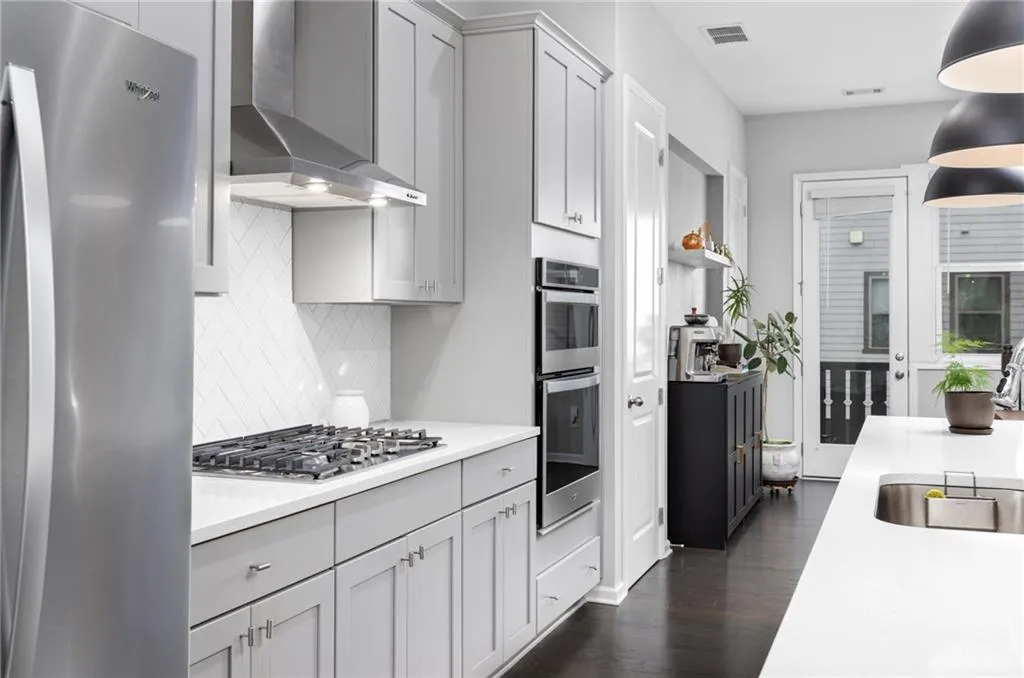 Kitchen featuring appliances with stainless steel finishes, wall chimney range hood, tasteful backsplash, dark wood-type flooring, and gray cabinets