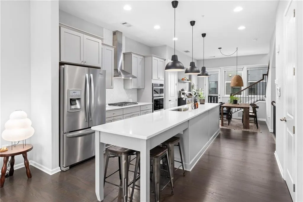 Kitchen with appliances with stainless steel finishes, decorative light fixtures, dark wood-style flooring, a kitchen bar, and gray cabinets