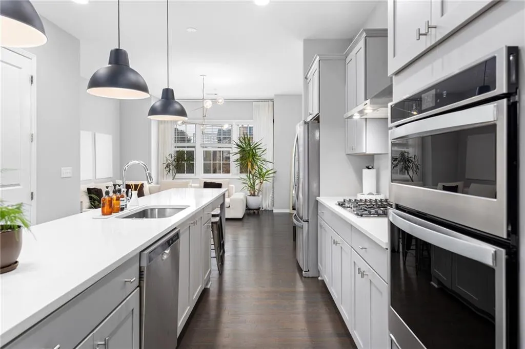 Kitchen featuring appliances with stainless steel finishes, pendant lighting, dark wood finished floors, light stone countertops, and gray cabinetry