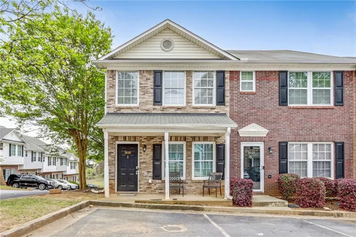 Exterior featuring a brick and stone facade, covered front porch, black paneled entry door, black shutters, and dedicated parking