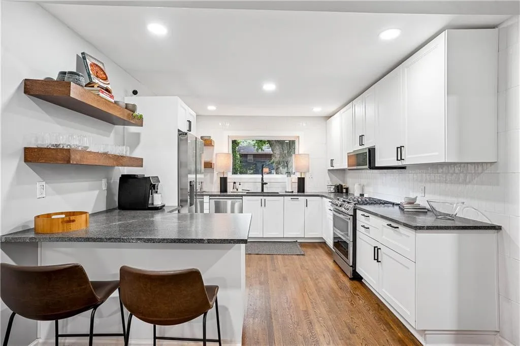 Kitchen featuring open shelves, dark wood-style flooring, a peninsula, a breakfast bar, and white cabinets