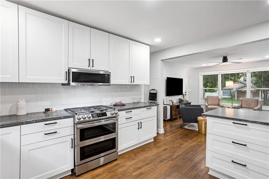 Kitchen with white cabinets, stainless steel appliances, decorative backsplash, open floor plan, and dark wood-type flooring