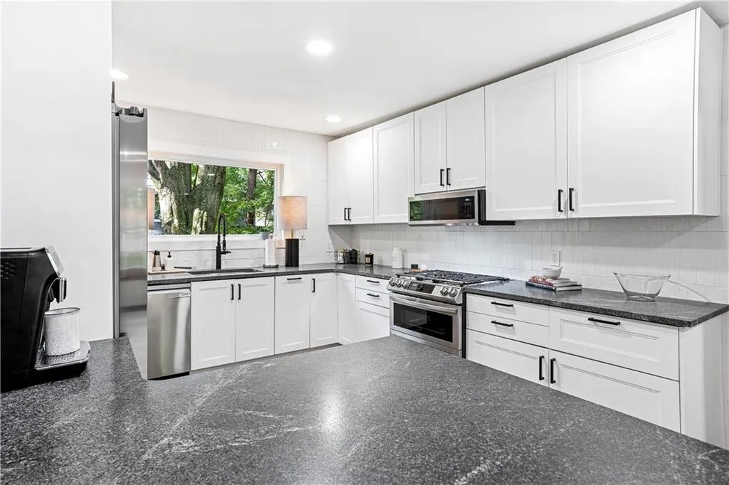 Kitchen with white cabinetry, backsplash, appliances with stainless steel finishes, recessed lighting, and dark stone countertops