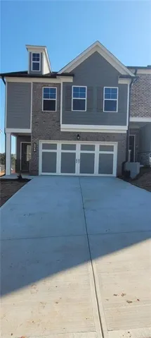 Contemporary townhome exterior featuring a two-car garage with white paneled doors, gray siding, and brick accents