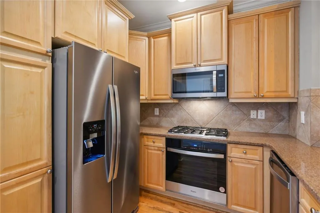 Kitchen with backsplash, light hardwood / wood-style floors, stainless steel appliances, and light stone countertops