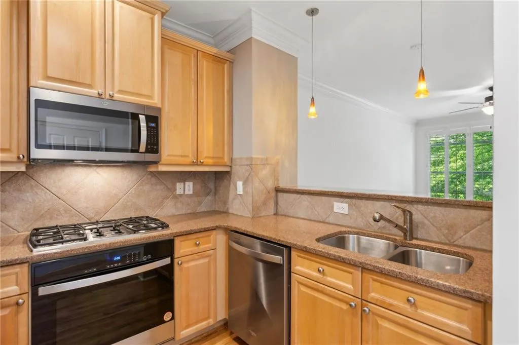 Kitchen featuring appliances with stainless steel finishes, ceiling fan, sink, tasteful backsplash, and hanging light fixtures
