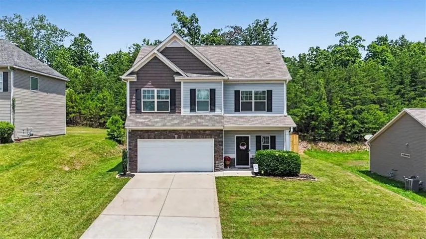 Two-story residential structure featuring multiple siding textures, an attached garage, and a concrete driveway