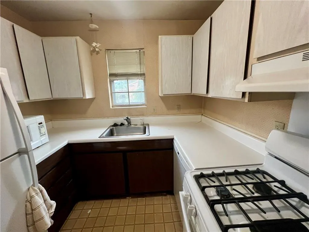 Kitchen featuring white appliances, under cabinet range hood, light countertops, and light tile patterned floors