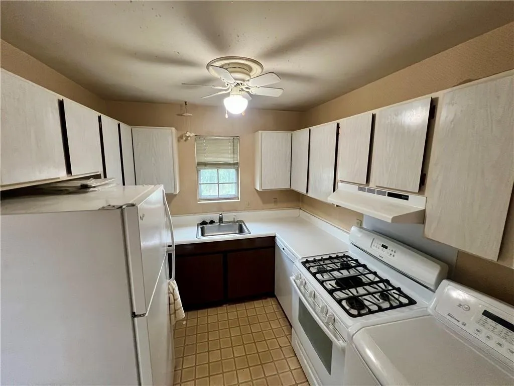 Kitchen featuring white appliances, under cabinet range hood, ceiling fan, washing machine and clothes dryer, and light countertops