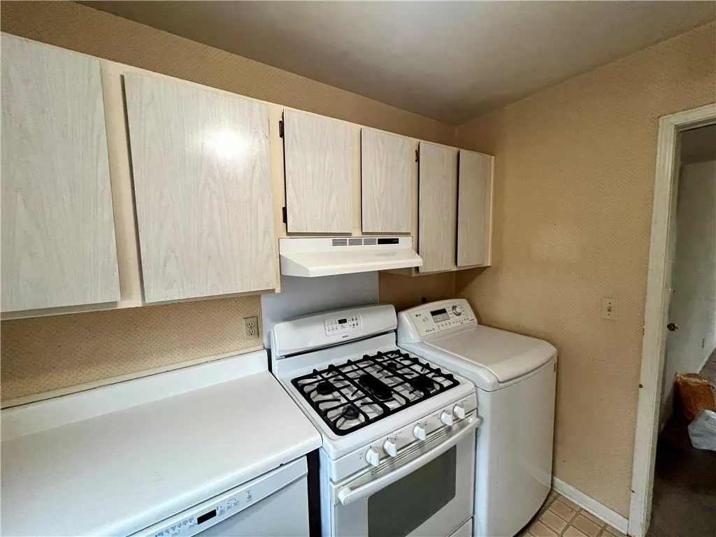 Kitchen featuring white appliances, under cabinet range hood, light countertops, light tile patterned floors, and washer and dryer