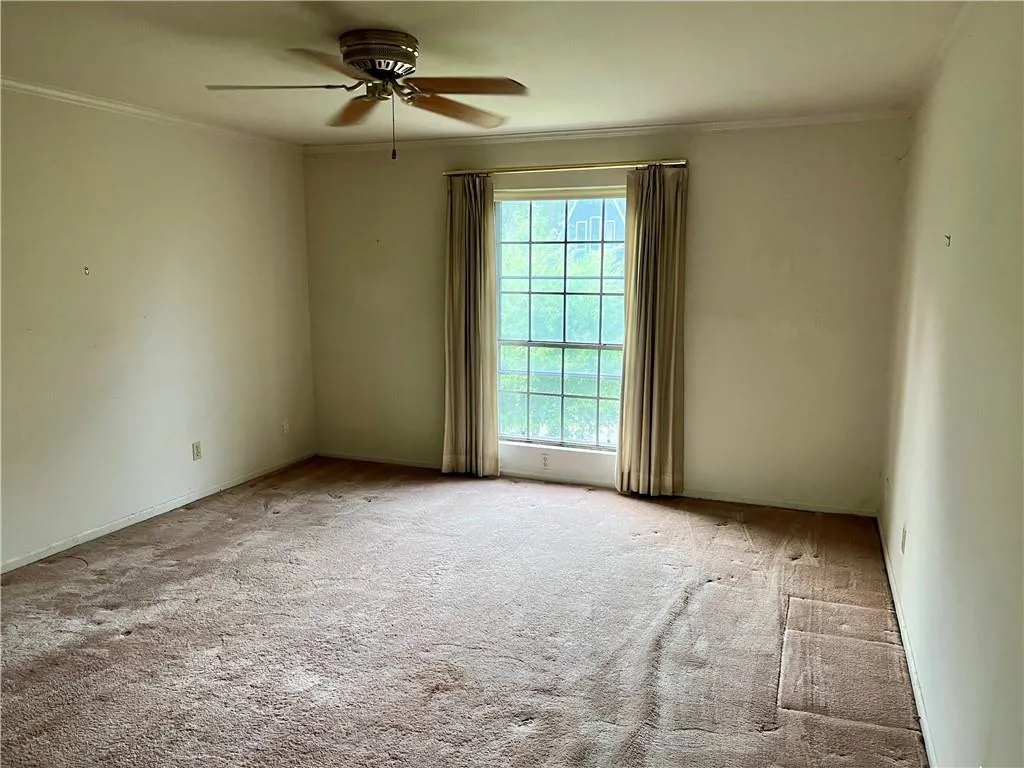 Carpeted empty room featuring ornamental molding and ceiling fan
