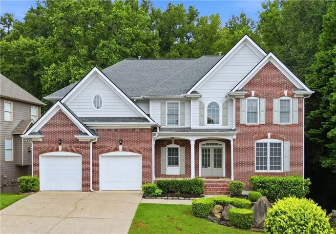 Traditional brick and siding exterior with a covered entry, dual garage doors, decorative shutters, mature landscaping, and an arched window