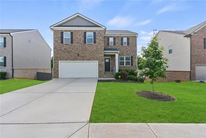 Two-story brick exterior featuring a two-car garage, a concrete driveway, and established front landscaping