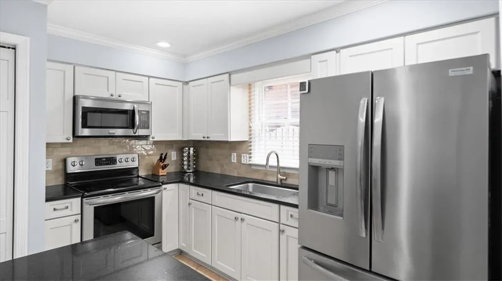 Kitchen featuring white cabinetry, backsplash, appliances with stainless steel finishes, sink, and crown molding