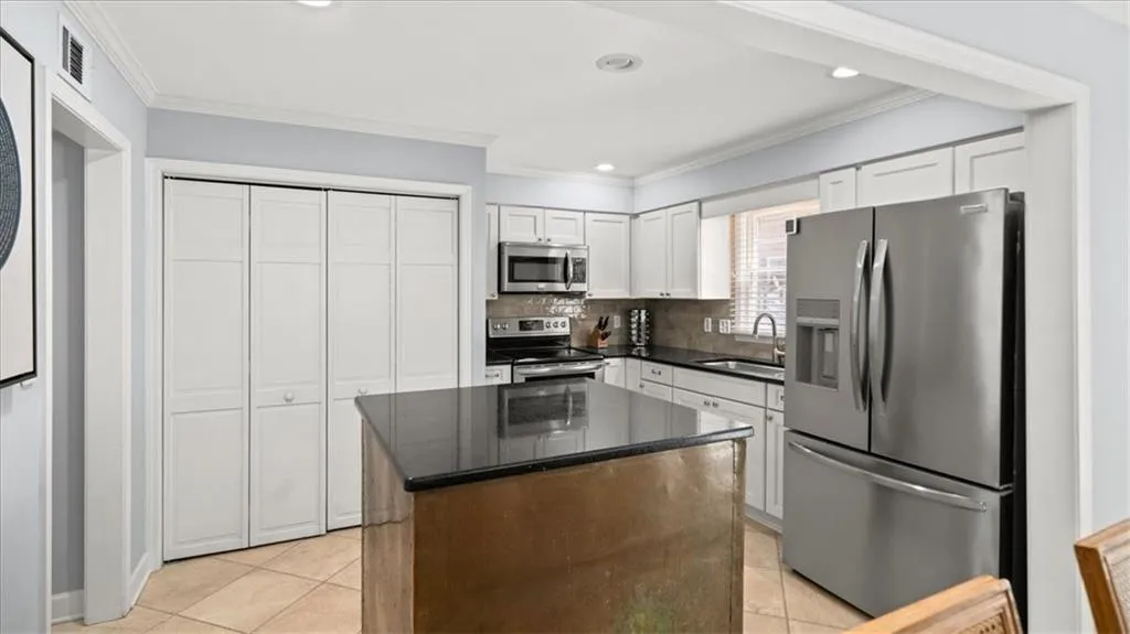Kitchen featuring appliances with stainless steel finishes, white cabinetry, light tile floors, a center island, and sink