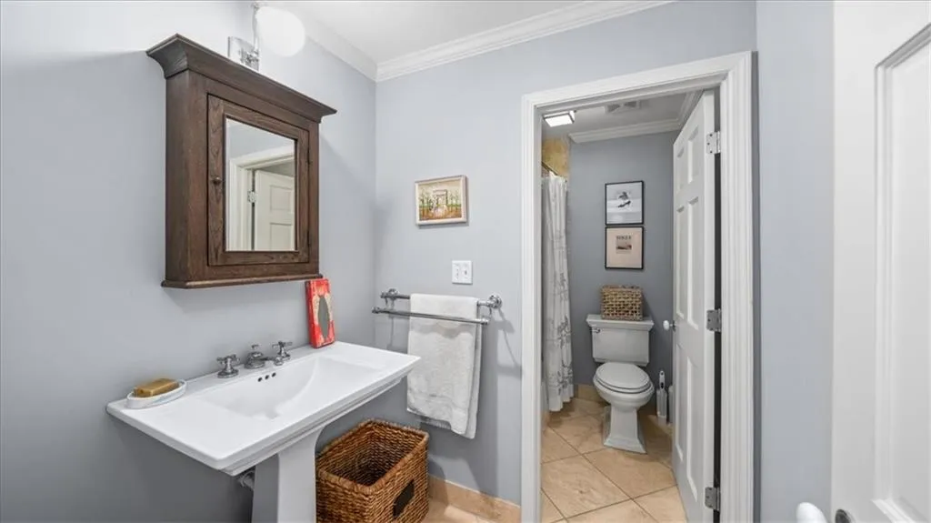 Bathroom featuring tile flooring, ornamental molding, toilet, and sink