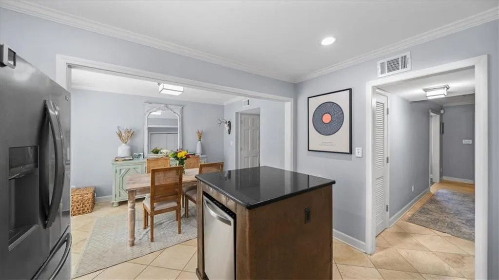 Kitchen featuring light tile floors, a center island, stainless steel refrigerator with ice dispenser, dark brown cabinets, and crown molding