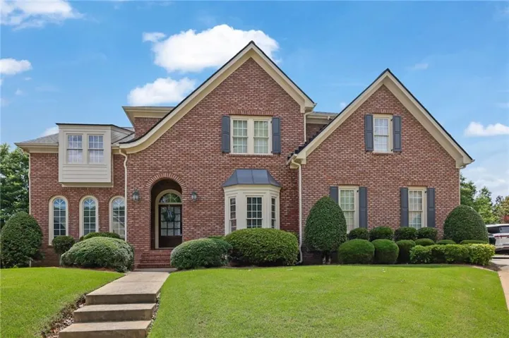 Brick exterior residence featuring a symmetrical facade, dark shutters, an arched entryway, a bay window, and a well-maintained lawn