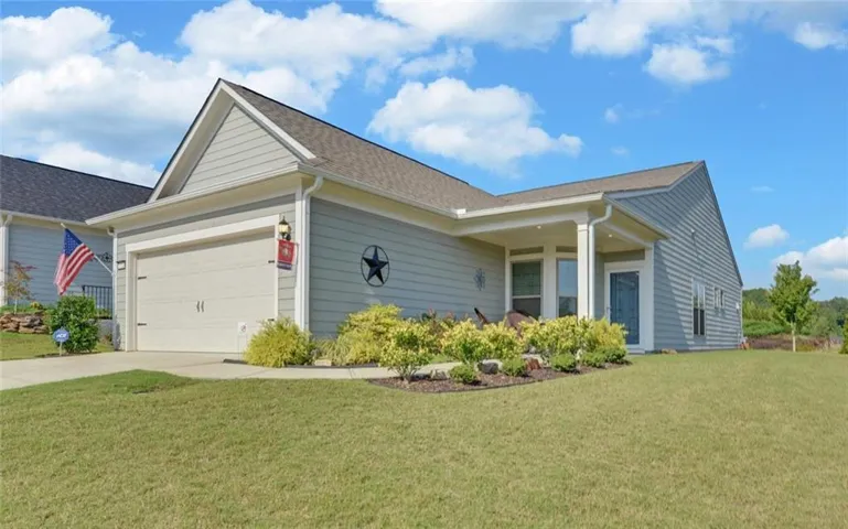 Light blue siding exterior with a covered entry, attached two-car garage, and established landscaping