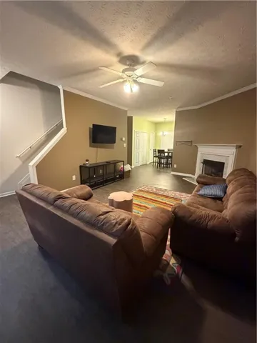 Living area featuring dark wood-finish flooring, a ceiling fan with light fixture, and a white fireplace surround