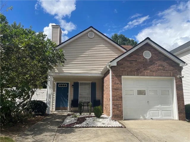 Brick and siding exterior with an attached garage, featuring a blue front door, white picket fence, and a landscaped front yard