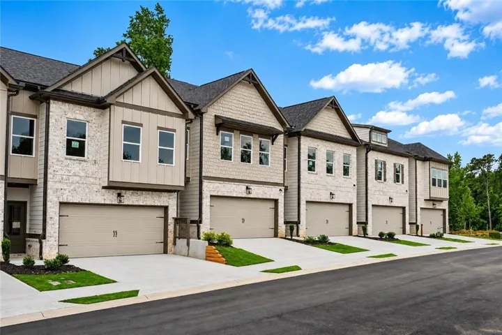 Contemporary townhomes featuring light-colored brick and siding exteriors, gabled roofs, two-car garages, and paved driveways