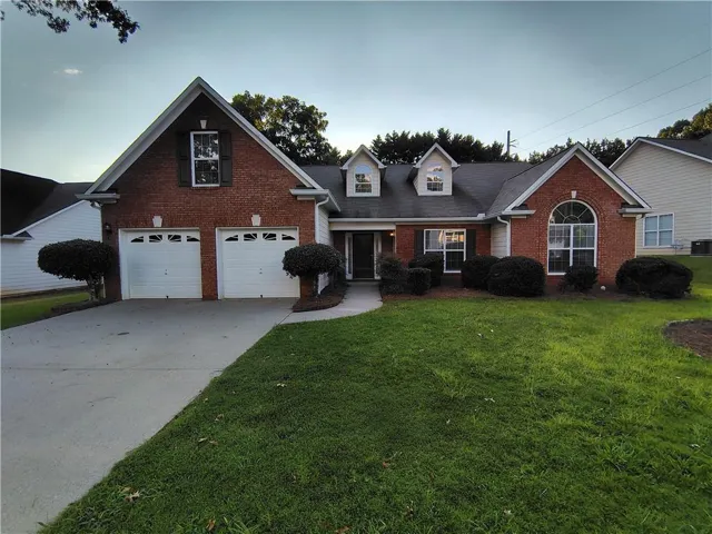 Brick exterior with white trim, a concrete driveway, two-car garage, and mature landscaping